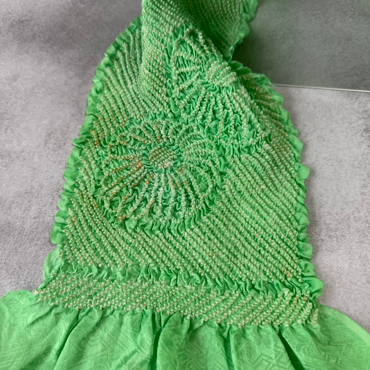Close-up of a floral shibori motif and visible age-related discolouration on a bright green silk obiage