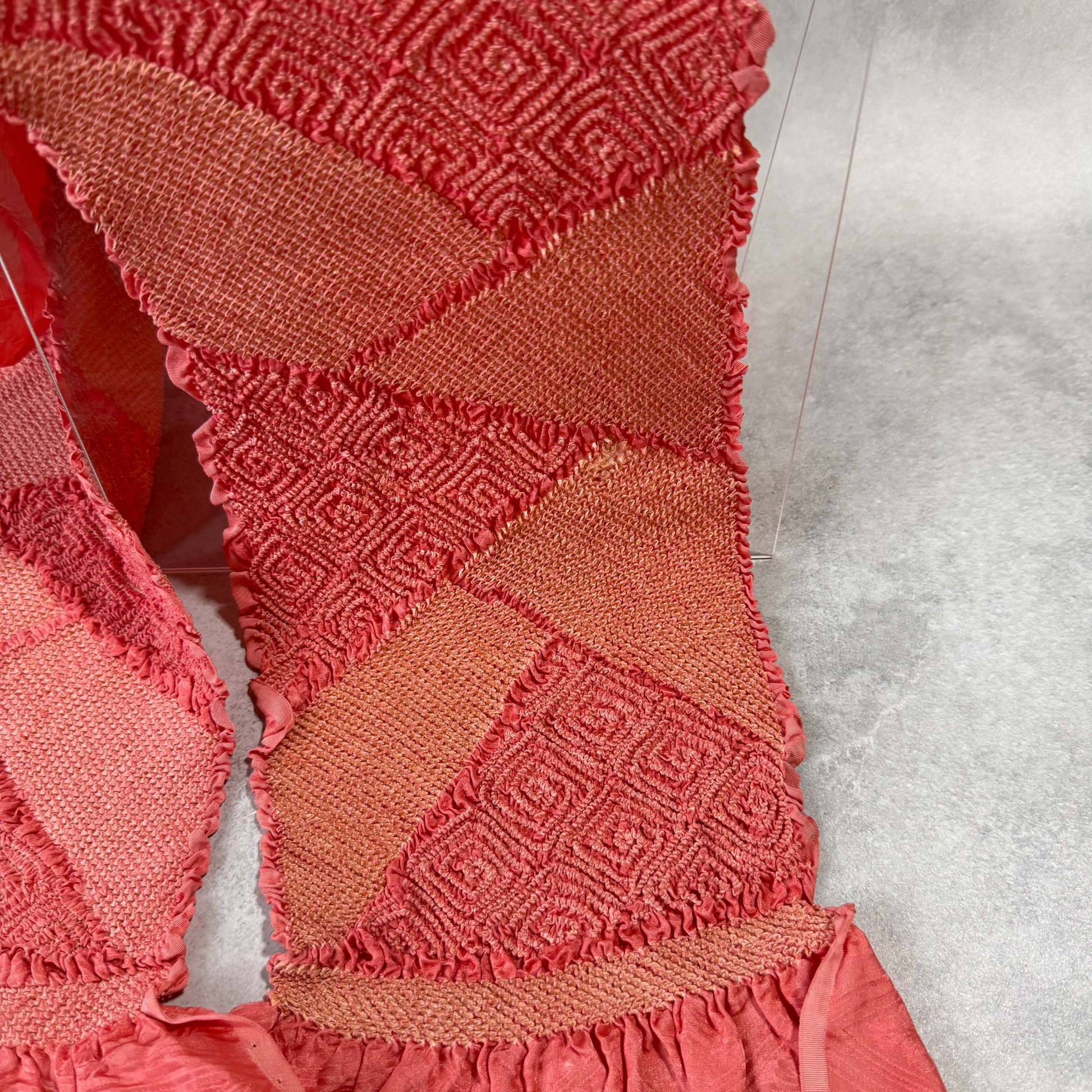 Close-up of geometric diamond shibori and diagonal panels on coral pink silk obiage