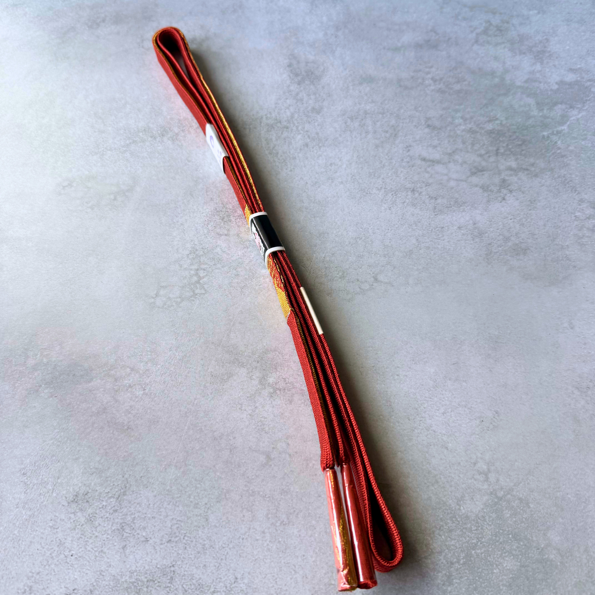 Both sides and protected tassel ends of the crimson red and gold Japanese silk obijime cord