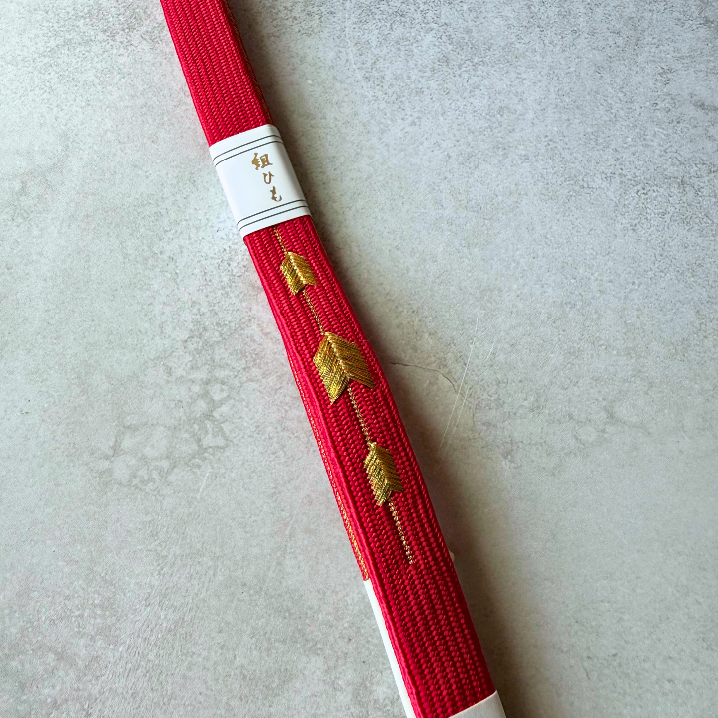 Close-up of metallic gold leaf-inspired motifs on a vivid crimson hand-braided silk obijime