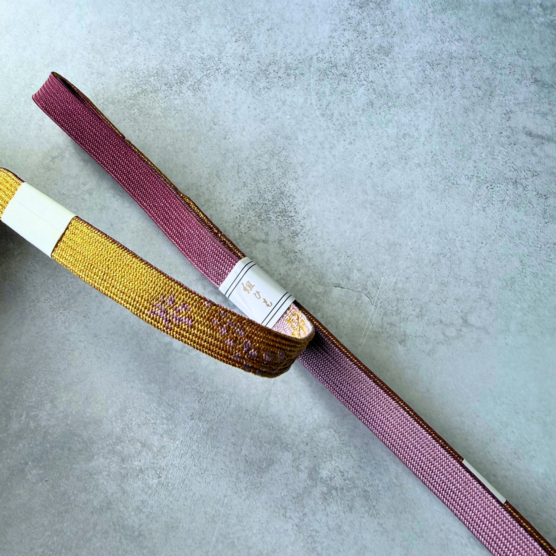 Close-up of gold and burgundy silk braiding and the original paper label on the unused obijime