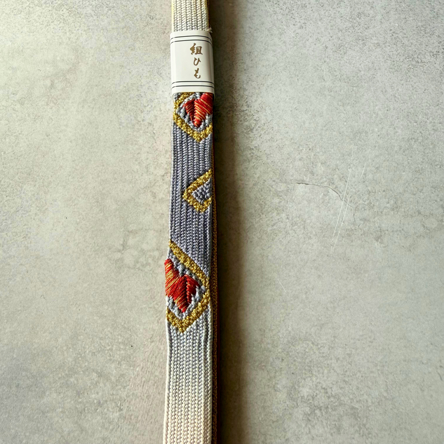 Close-up of the hand-braided Korai-gumi obijime with red and gold geometric motifs on a silver-gray and white ground.