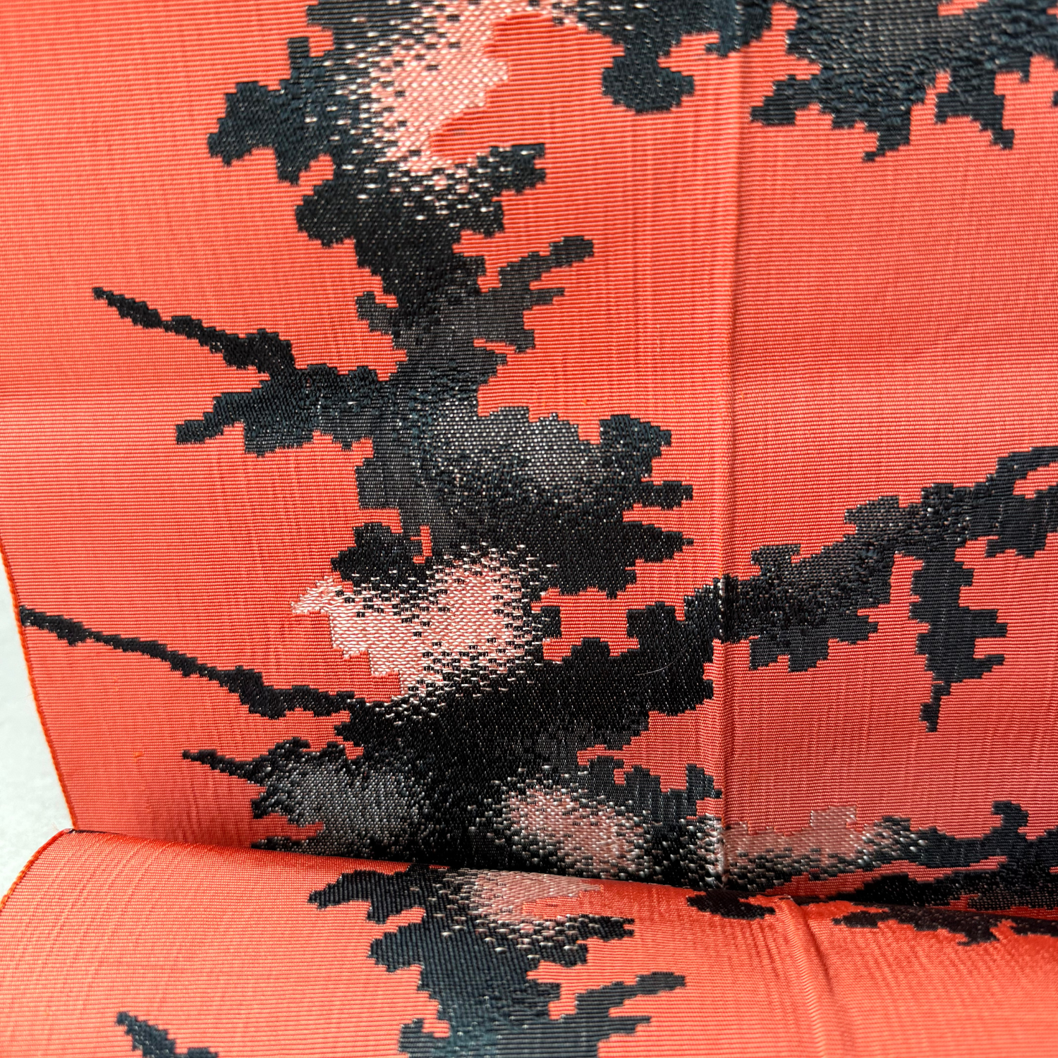 Close-up of abstract black and pale pink weaving on coral rayon obi fabric