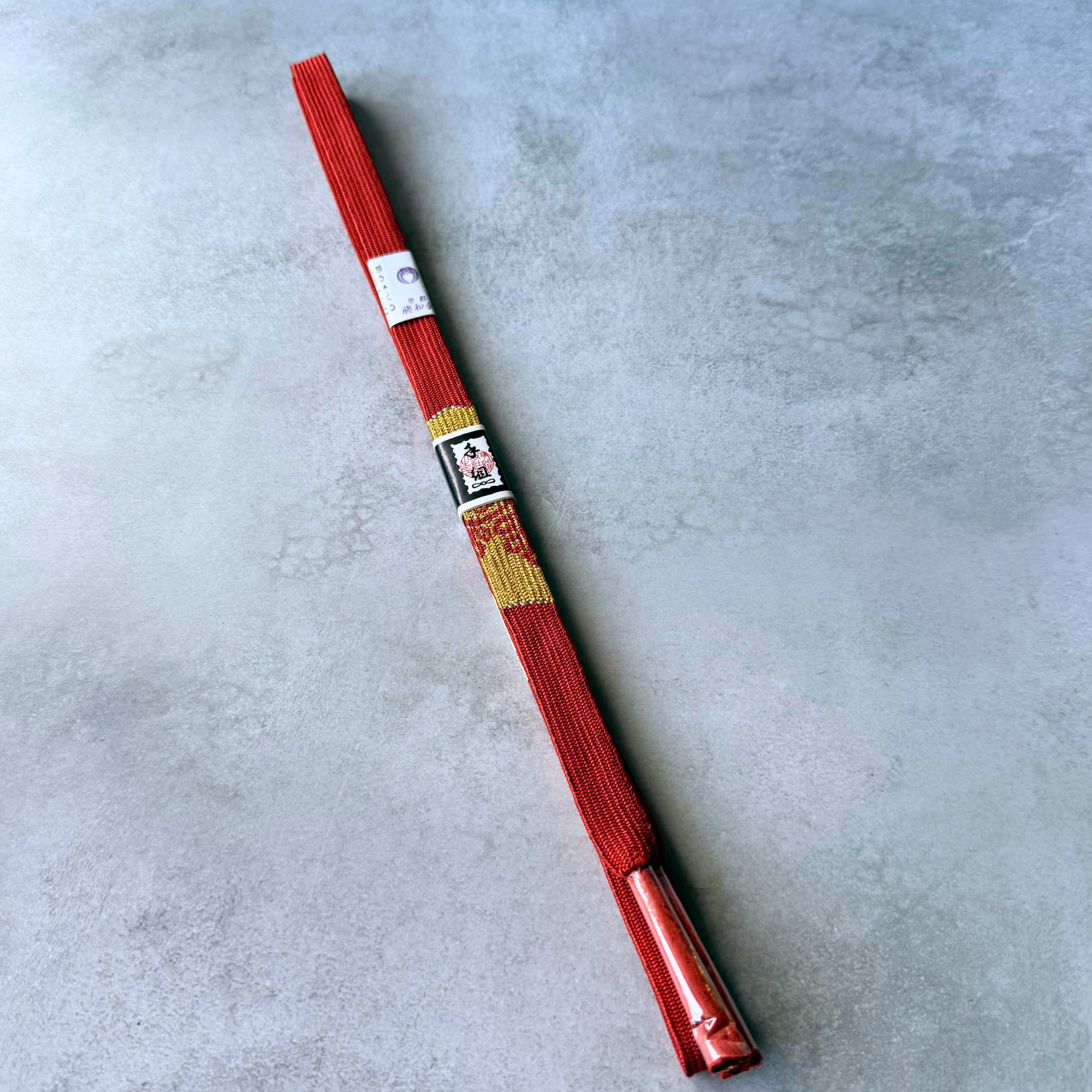 Full view of an unused Japanese hand-braided silk obijime cord in crimson red and metallic gold