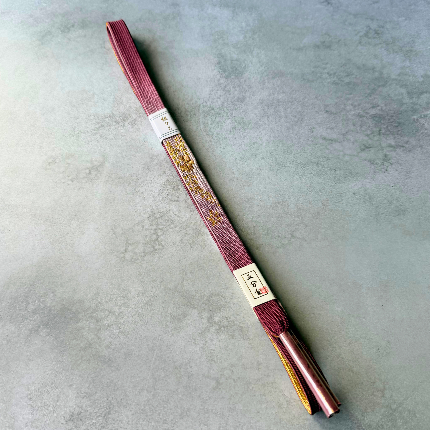 Full view of an unused Japanese hand-braided silk obijime cord in dusty pink, burgundy and gold