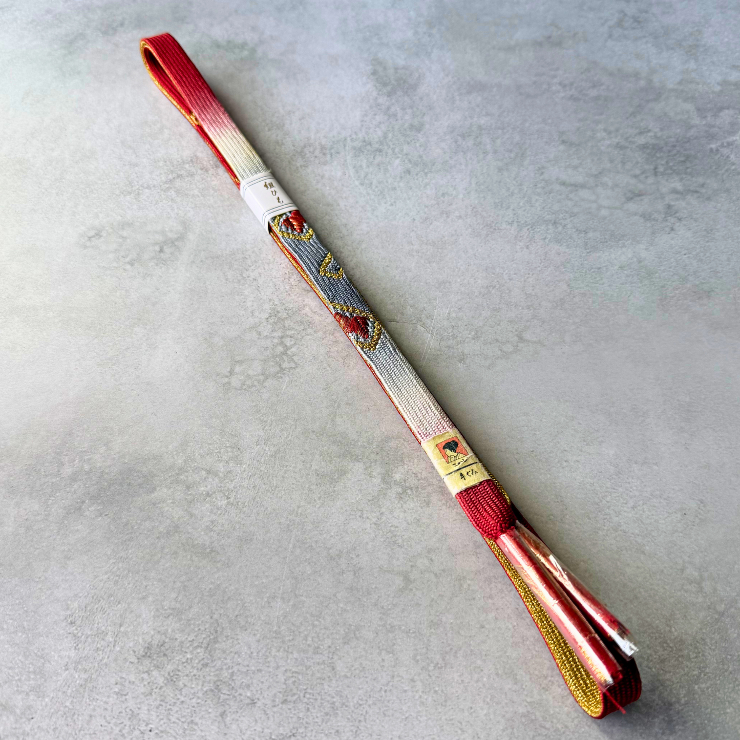 Unused Japanese silk Korai-gumi obijime in red, silver, white and gold, shown in a full folded view.