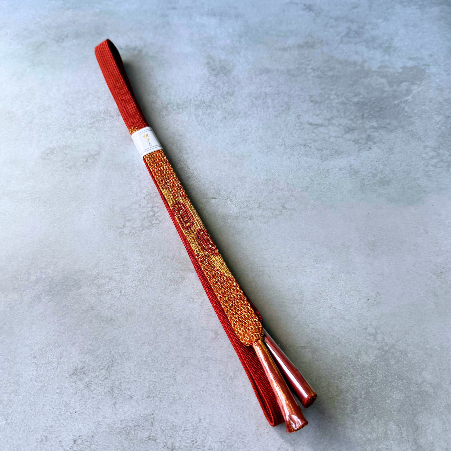 Full view of an unused Japanese silk Korai-gumi obijime in vermilion red and metallic gold
