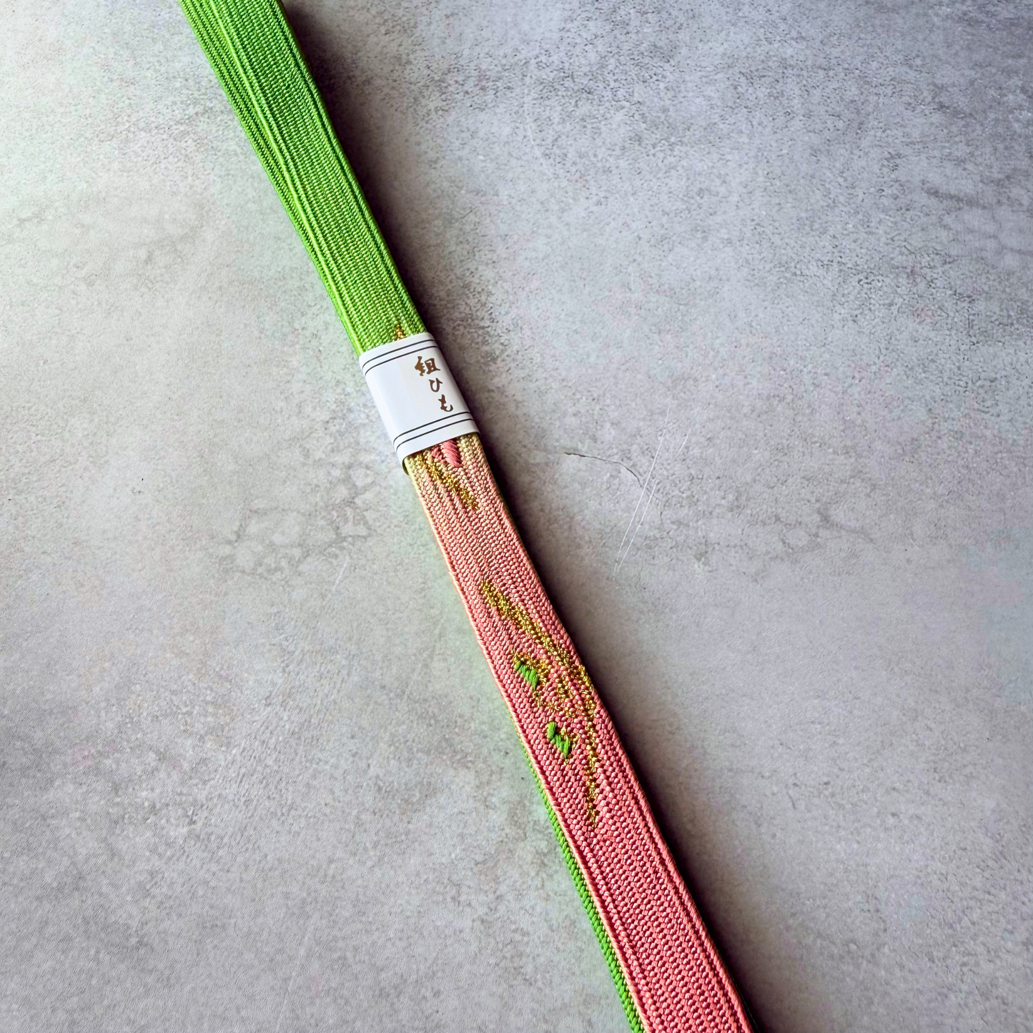 Close-up of blush pink section with metallic gold and green flowing motifs on Japanese silk obijime