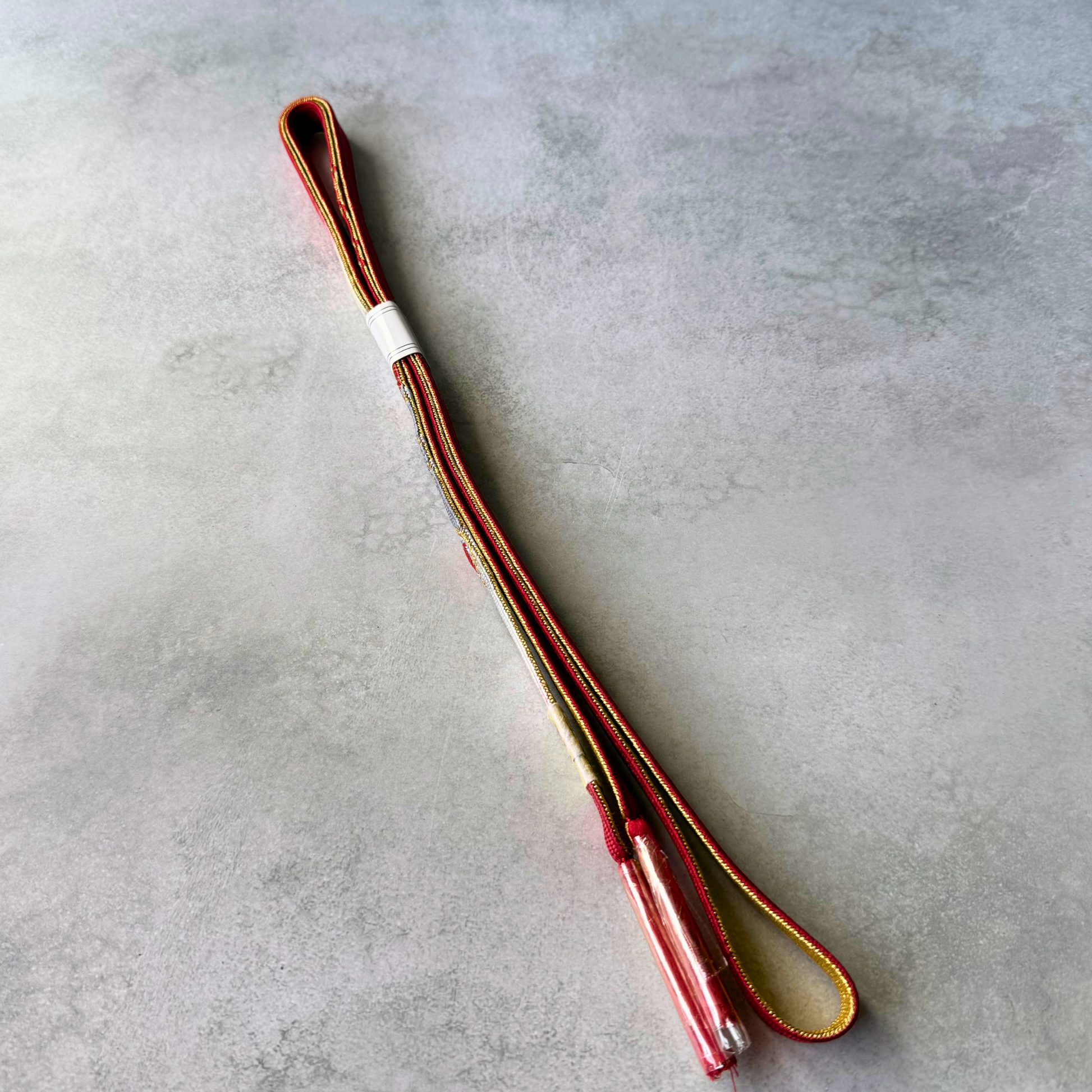 Side view of the Japanese silk obijime showing red and gold edging and the protected tassel ends.