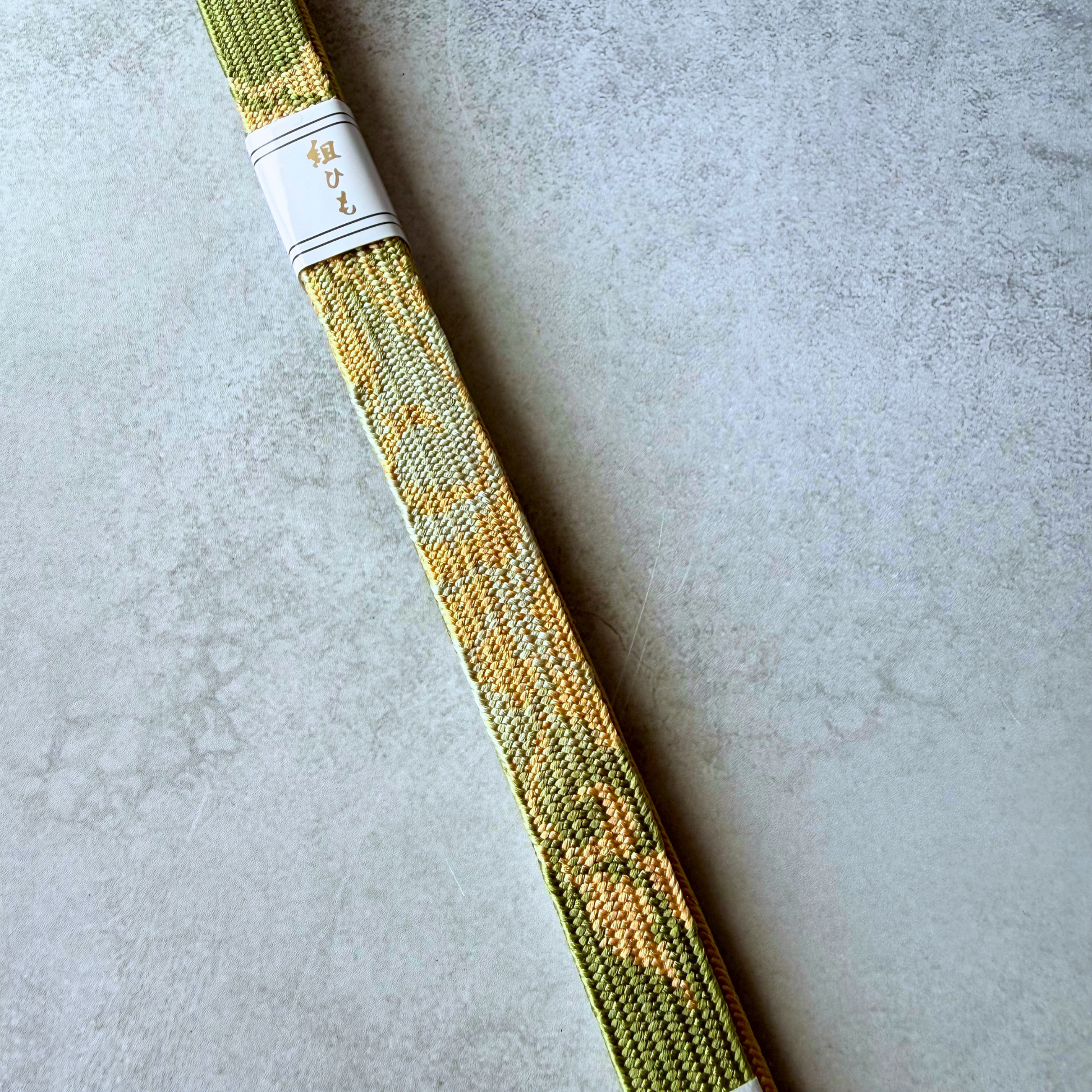 Close-up of gold geometric pattern on olive green hand-braided silk obijime