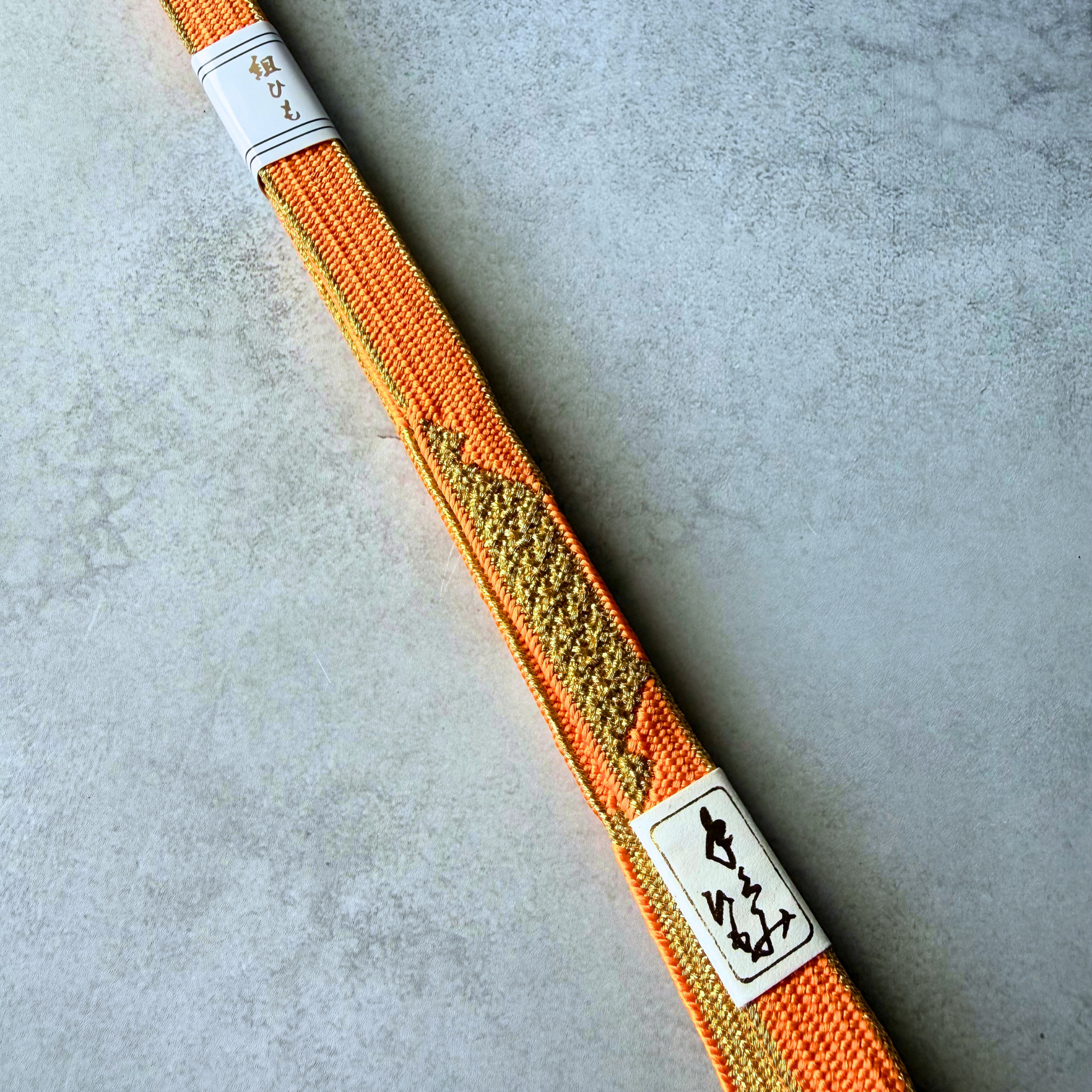 Close-up of the gold geometric pattern and hand-braided texture on an orange silk obijime