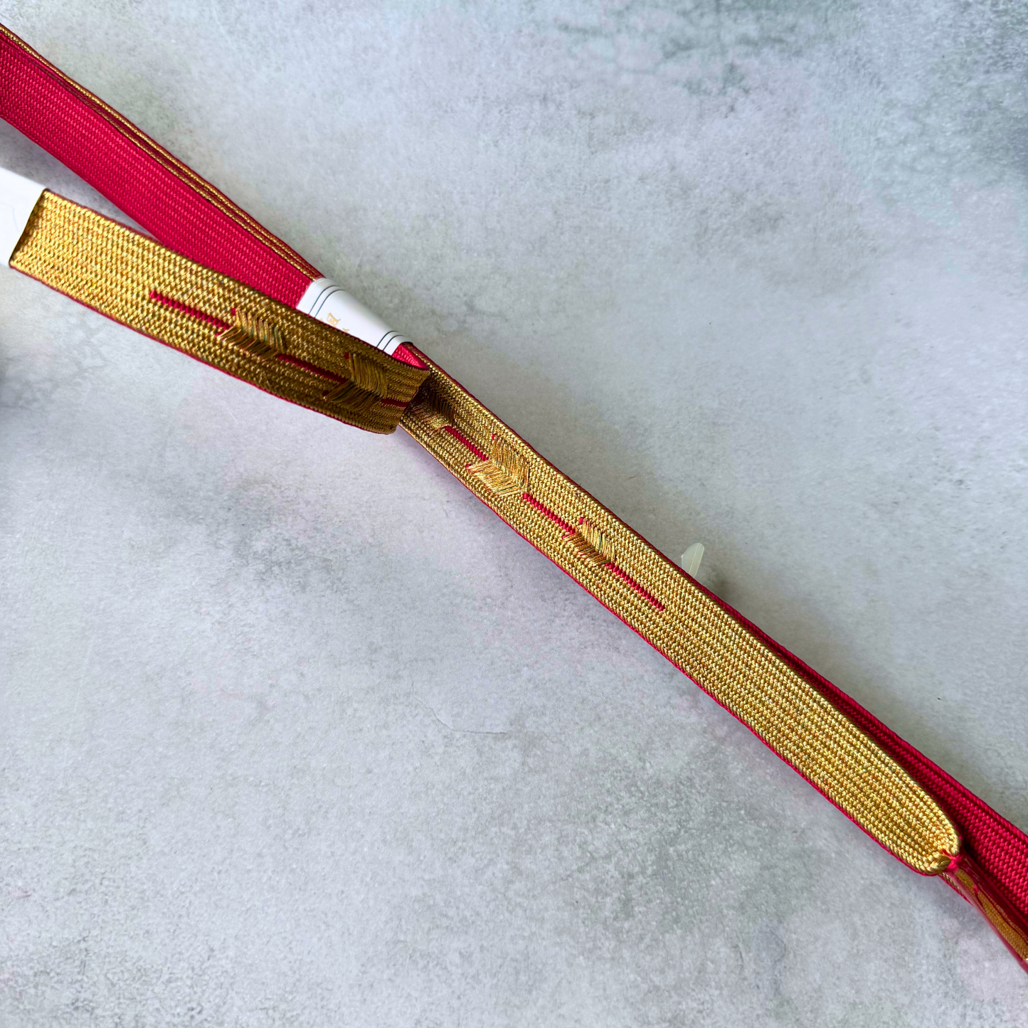 Detailed view of the metallic gold reverse and crimson edges of a hand-braided Korai-gumi obijime
