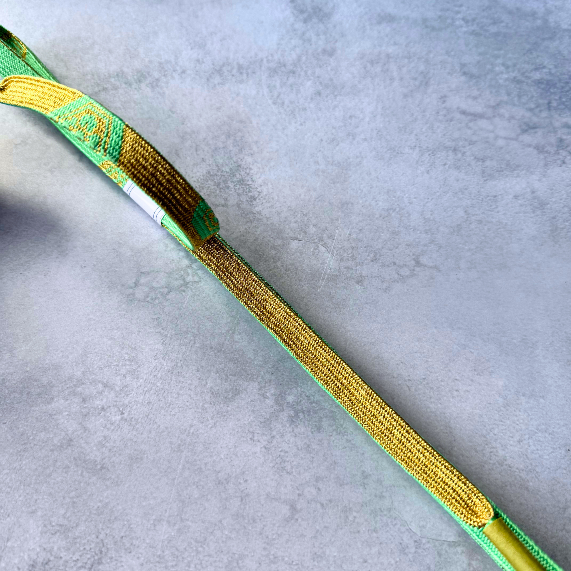 Detailed view of the metallic gold reverse and spring green edging on a hand-braided silk obijime