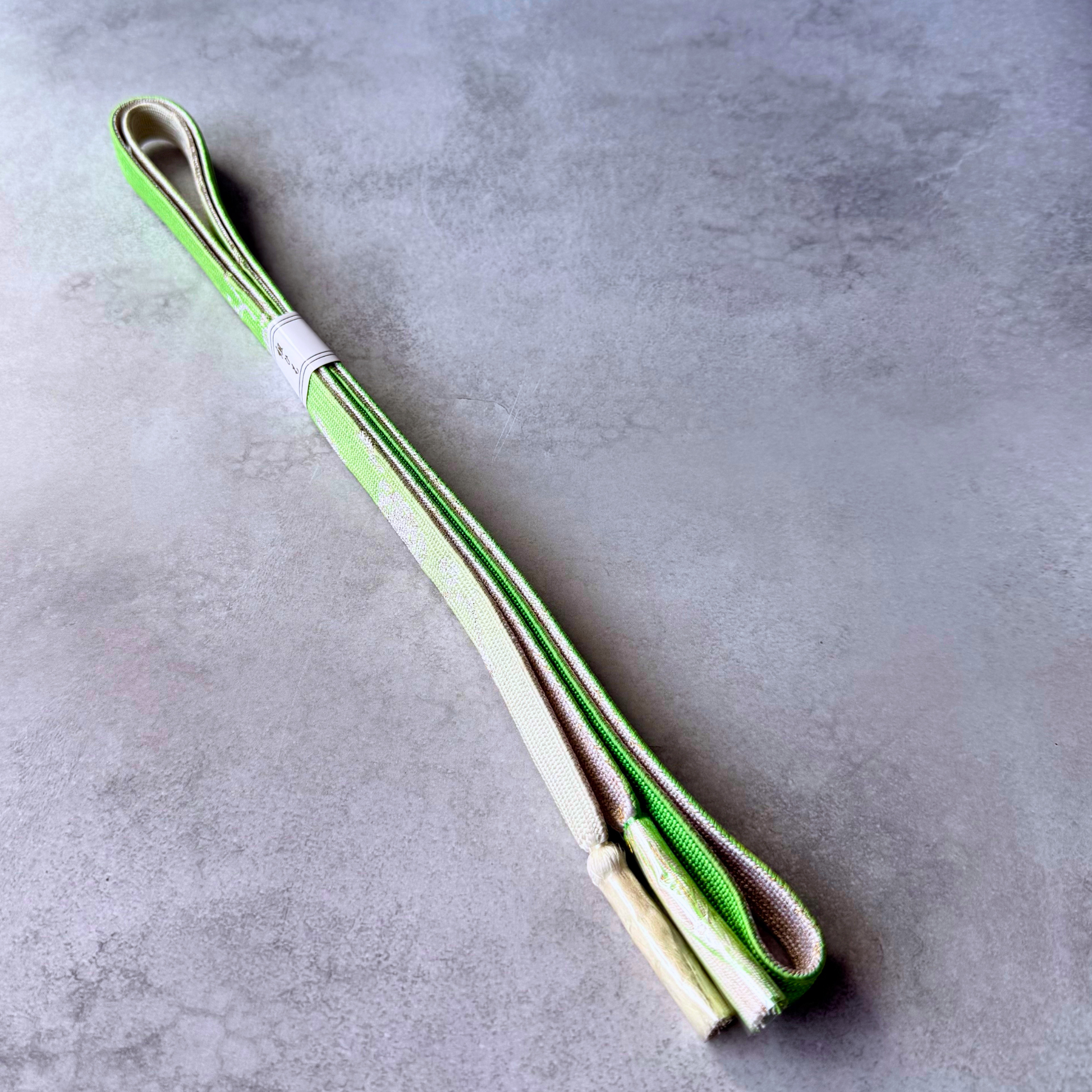 Folded Japanese Korai-gumi obijime showing lime green, ivory and pale gold sides with silk tassels