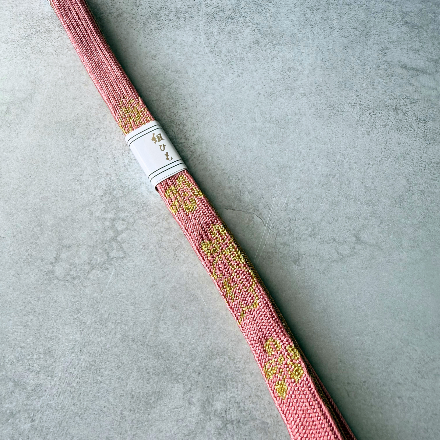 Close-up of metallic gold flowing decorative motifs woven into dusty rose silk obijime