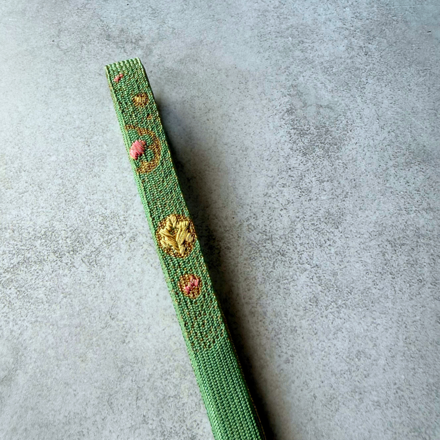 Detailed close-up of pink and metallic gold woven ornament on celadon green obijime
