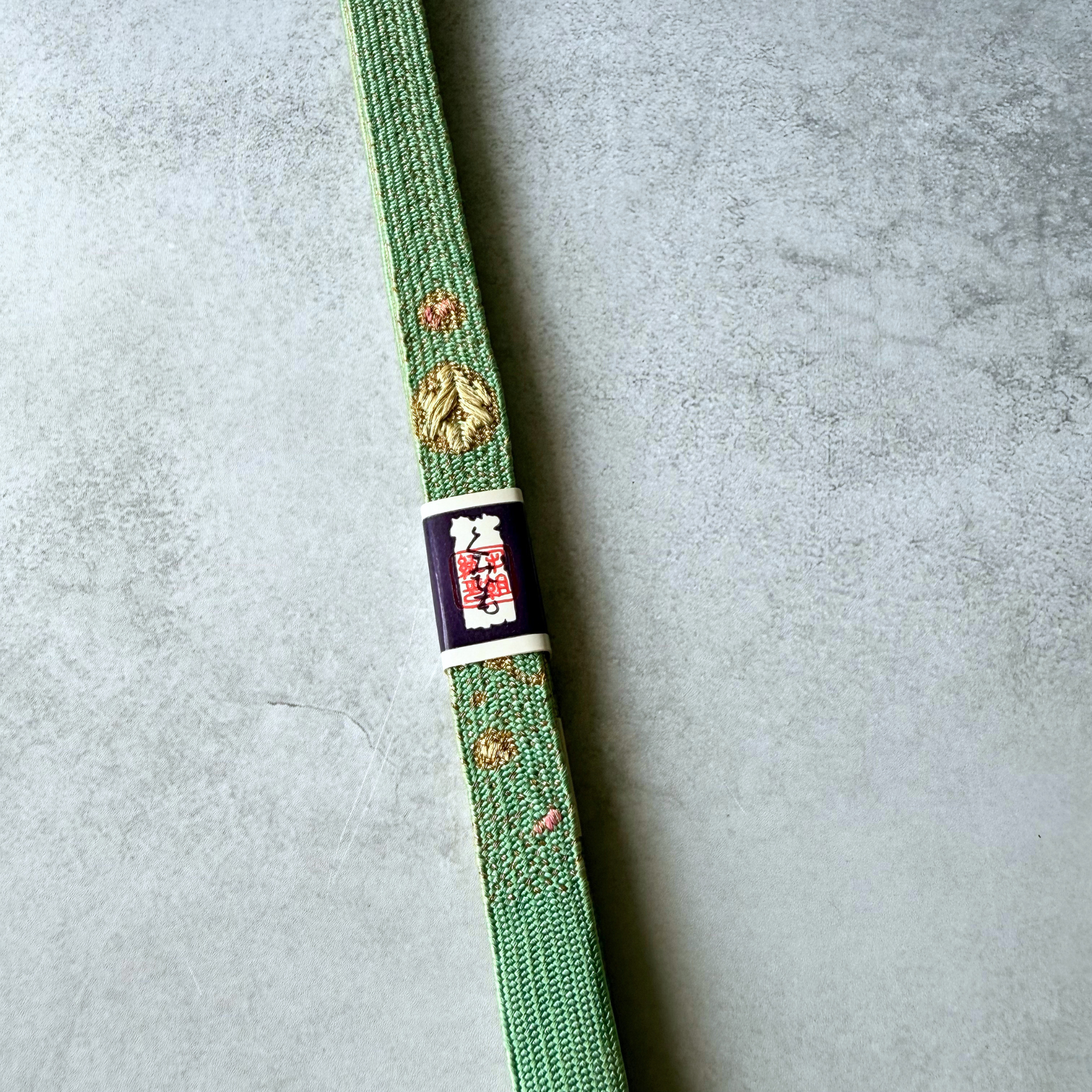 Close-up of gold and pink decorative woven motifs on celadon green silk obijime