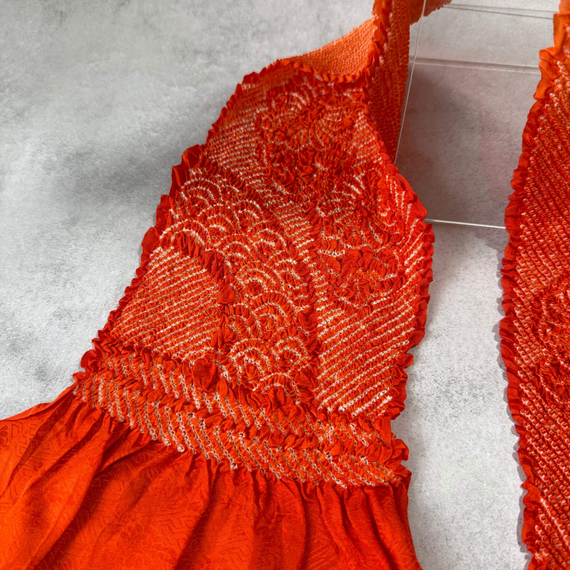 Detailed view of white shibori lines forming floral and wave-like patterns on orange silk