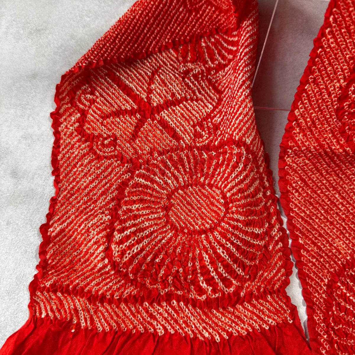 Detailed view of chrysanthemum-like shibori pattern on red silk obiage