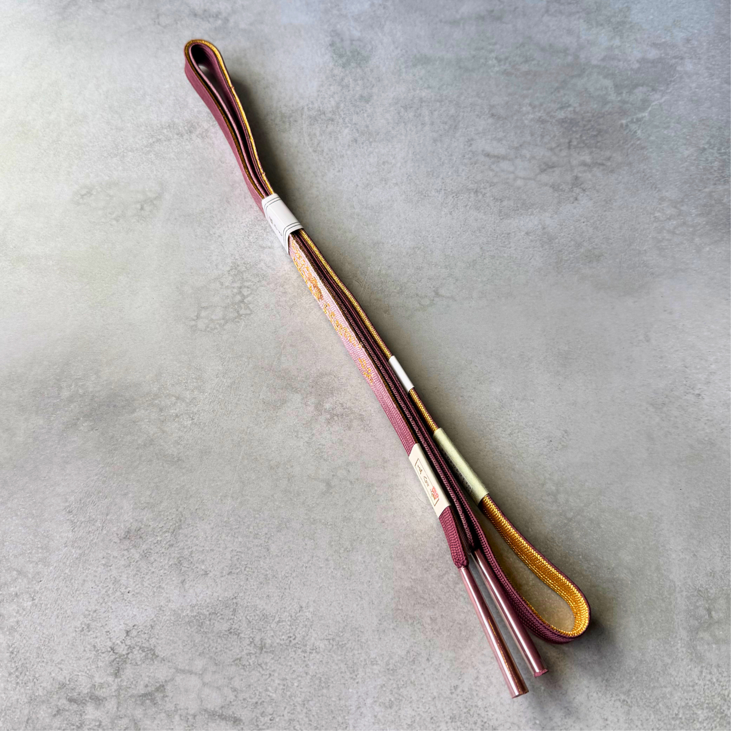 Both sides of the reversible silk obijime showing dusty pink, burgundy and gold color variations
