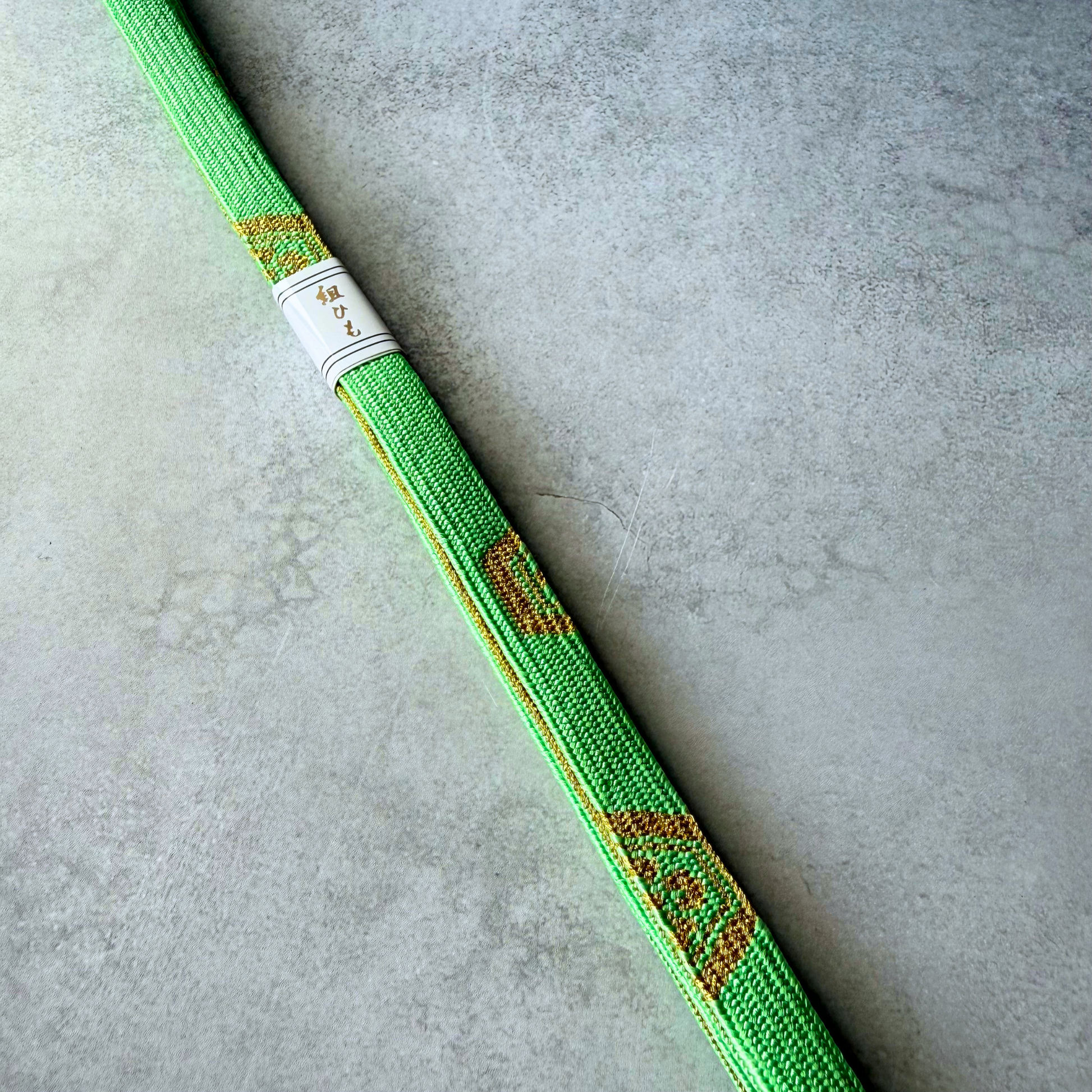 Close-up of metallic gold geometric motifs woven into a bright spring green silk Korai-gumi obijime
