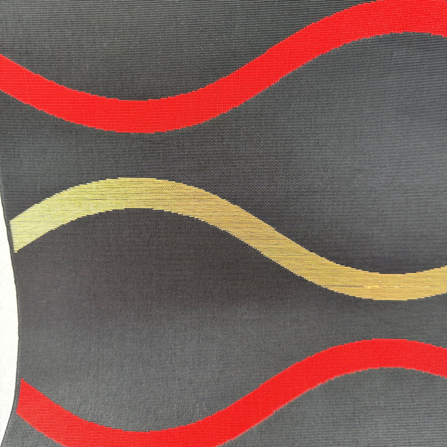 Close-up of red and gold horizontal wave bands on black obi fabric