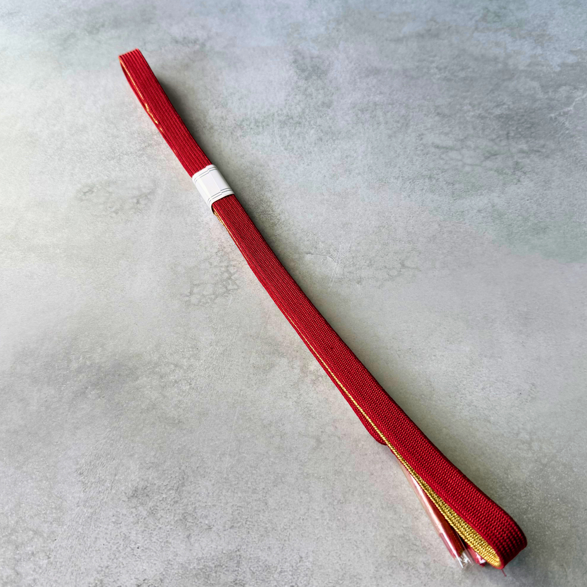 Reverse side of the unused silk obijime, featuring a vivid red braided surface with fine gold edging.