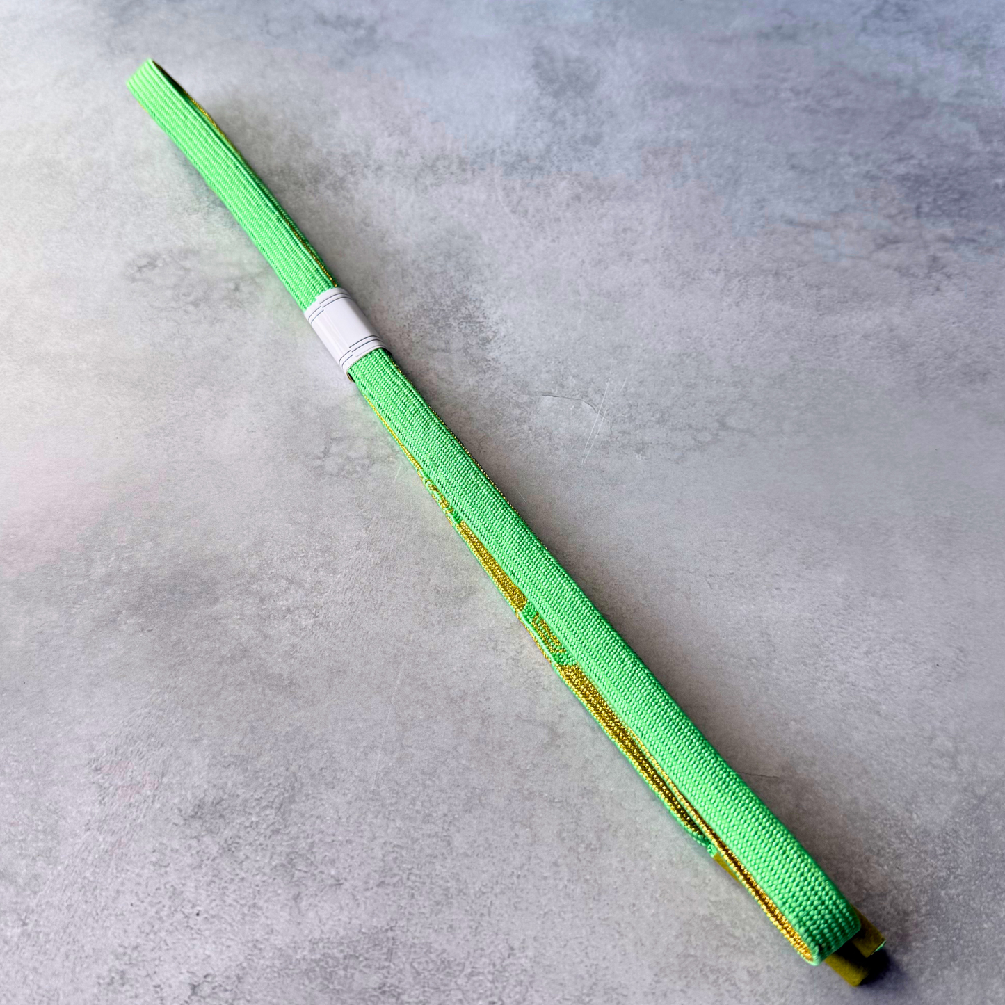 Plain bright spring green side and original paper label of an unused Japanese silk obijime