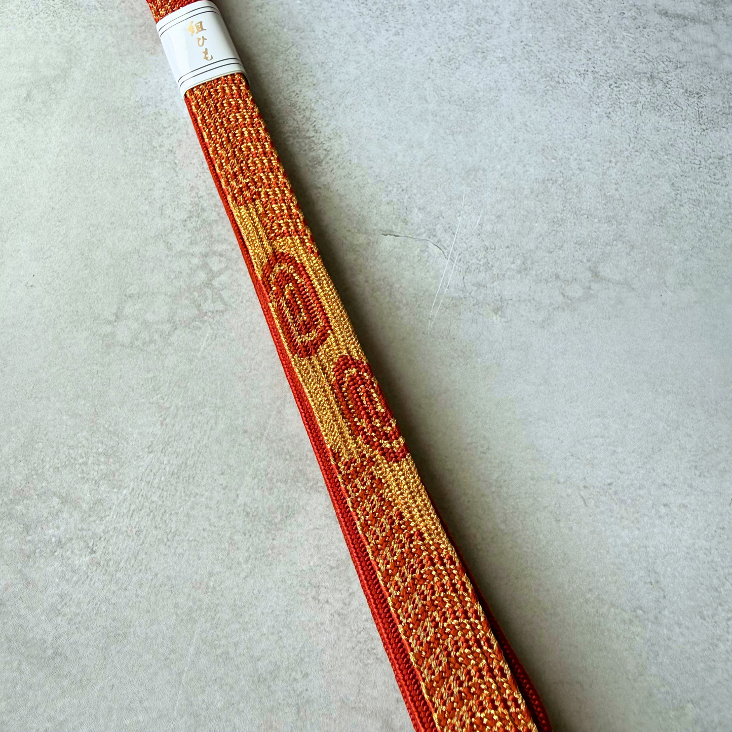 Close-up of metallic gold braiding and red circular geometric motifs on a silk obijime