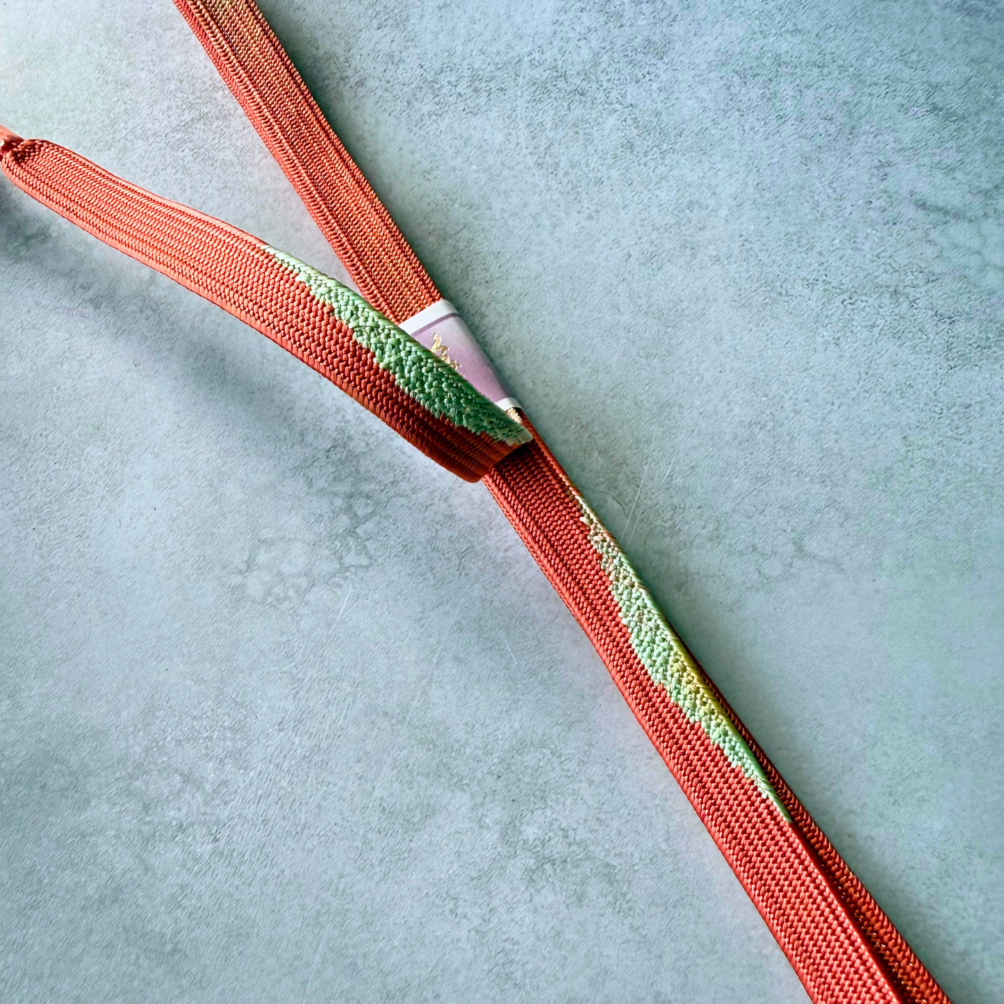Detailed view of vermilion, pale green and gold silk braiding on Japanese kumihimo obijime