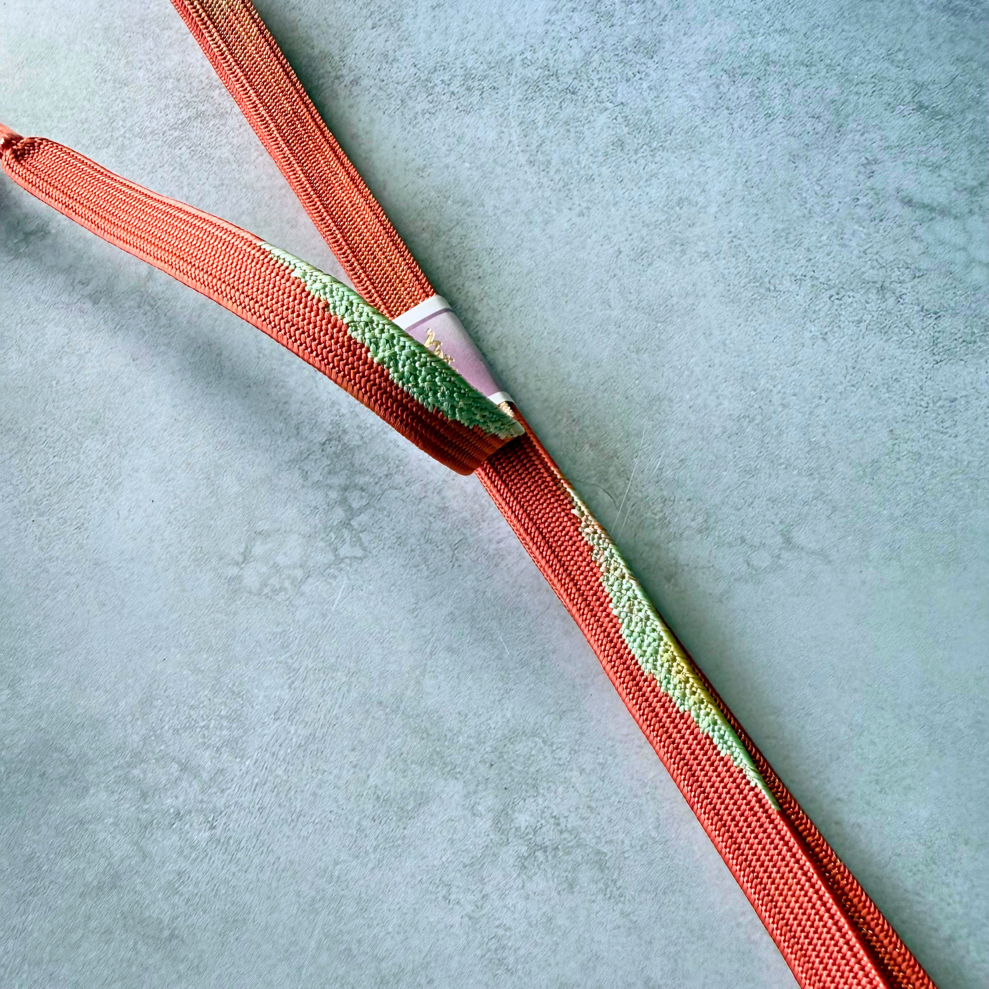 Detailed view of vermilion, pale green and gold silk braiding on Japanese kumihimo obijime