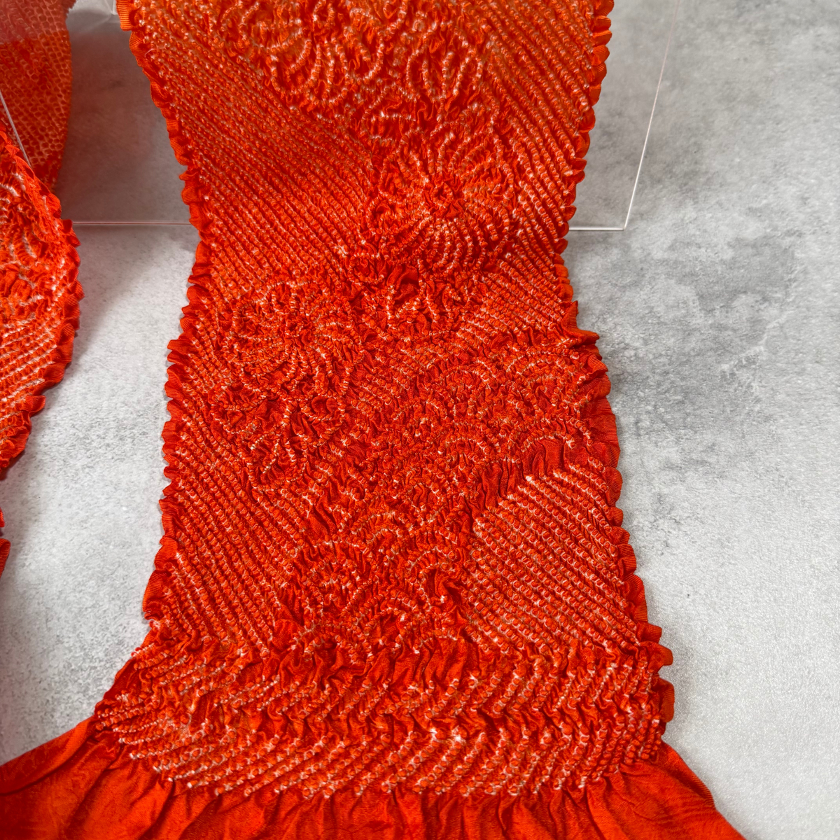 Close-up of floral and wave-like shibori motifs on vermilion orange silk
