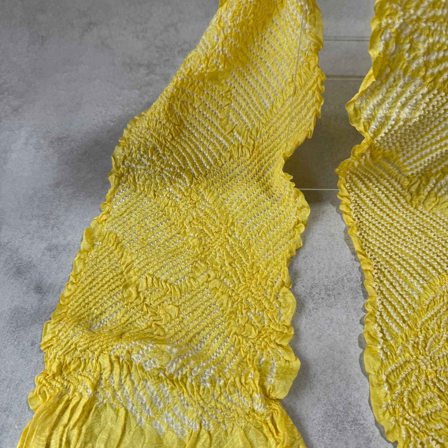 Detailed view of white shibori lines and floral designs on a yellow silk obiage